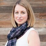 Kellie, founder of The Yuppie Files, wearing a plaid scarf and white top, standing against a wooden background.